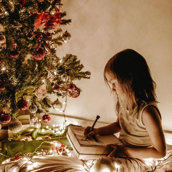 girl sitting in front of christmas tree and tree lights, drawing