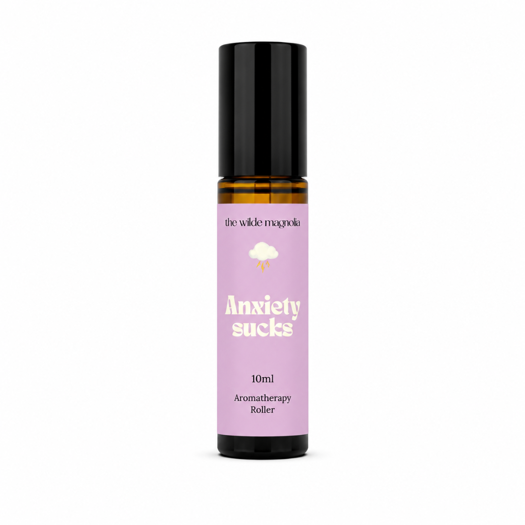 A 10ml amber glass roll-on bottle with a black cap and a lavender purple label that reads 'Anxiety sucks' by the brand 'the wilde magnolia'.