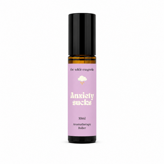 A 10ml amber glass roll-on bottle with a black cap and a lavender purple label that reads 'Anxiety sucks' by the brand 'the wilde magnolia'.