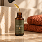 Amber dropper bottle with olive green label saying "Beard & Skin Conditioning Oil. Cedarwood + Vetiver" on travertine stone with warm lighting with dropper held over the opening