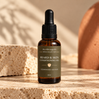 Amber dropper bottle with olive green label saying "Beard & Skin Conditioning Oil. Cedarwood + Vetiver" on travertine stone with warm lighting