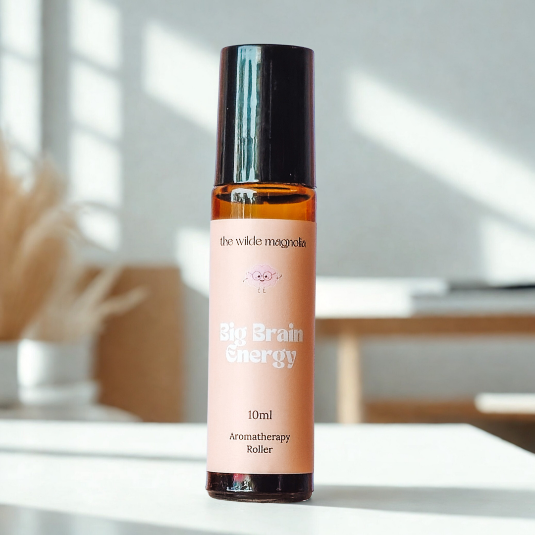 Aromatherapy roller bottle labeled 'Big Brain Energy' by 'the wilde magnolia' on a white surface with a blurred indoor background.
