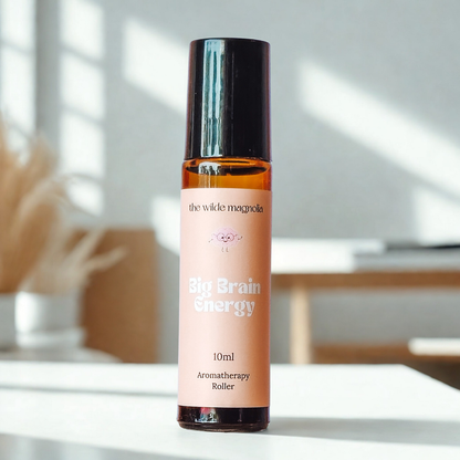 Aromatherapy roller bottle labeled 'Big Brain Energy' by 'the wilde magnolia' on a white surface with a blurred indoor background.