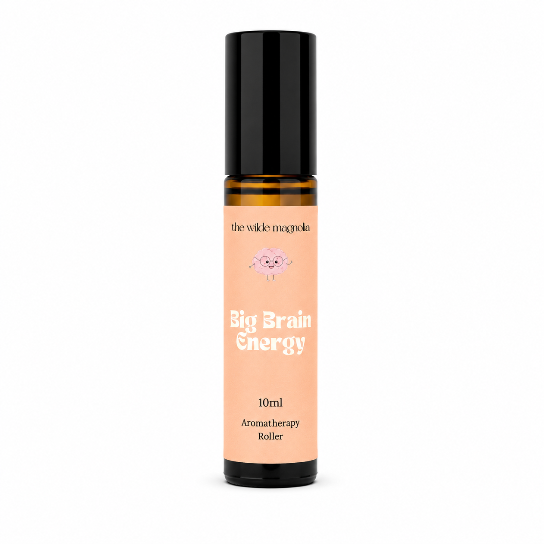 A 10ml aromatherapy roller bottle with a black cap and a peach-colored label. The label features the brand name 'the wilde magnolia' and the product name 'Big Brain Energy' in white text.