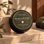 A round black tin with an olive-green label titled "Beard Softener, Cedarwood + Vetiver" by The Wilde Magnolia Sitting on travertine stone with olive green accents