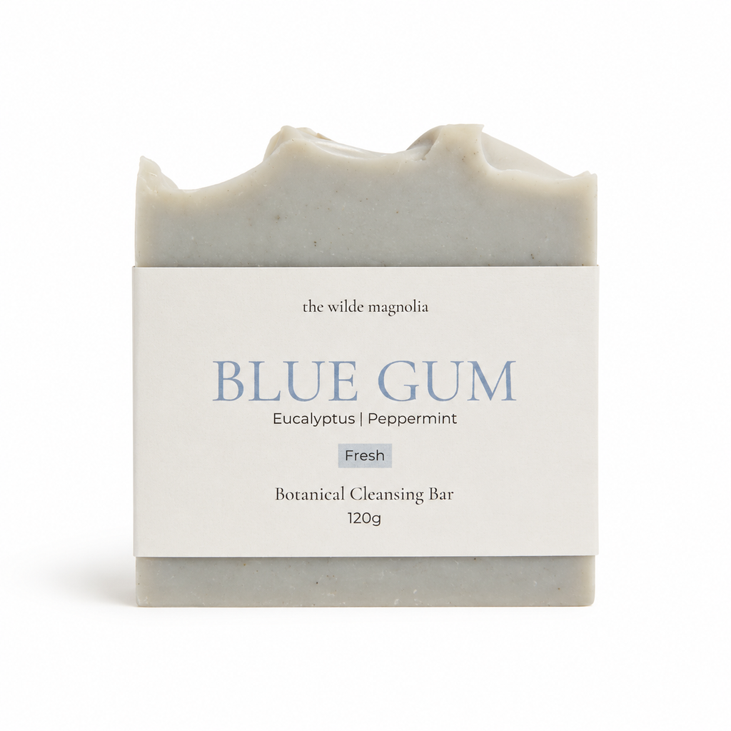 A rectangular bar of soap by 'The Wilde Magnolia' wrapped in a white paper label that reads 'BLUE GUM' with 'Eucalyptus | Peppermint' and 'Fresh' underneath, on a clean white background.