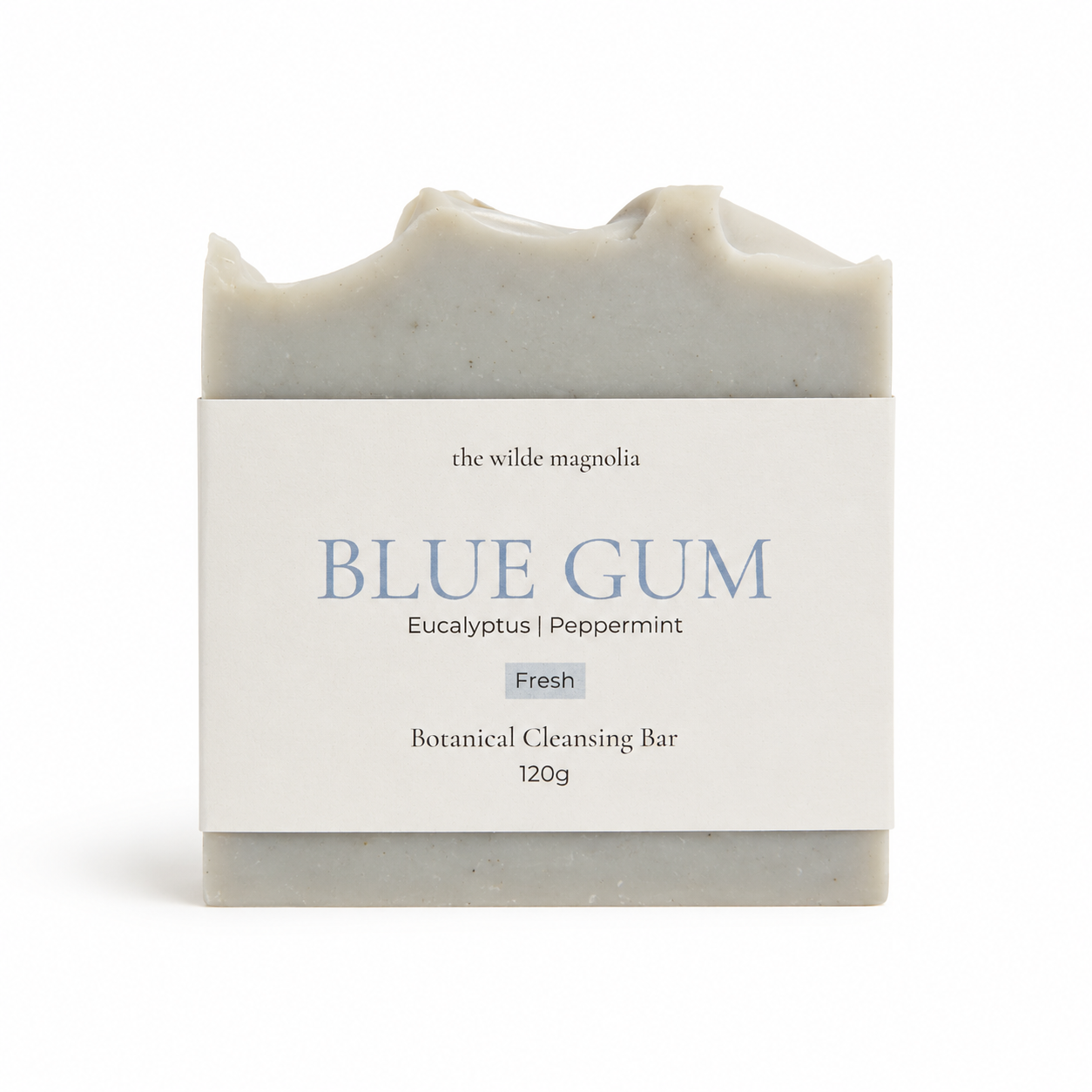 A rectangular bar of soap by 'The Wilde Magnolia' wrapped in a white paper label that reads 'BLUE GUM' with 'Eucalyptus | Peppermint' and 'Fresh' underneath, on a clean white background.