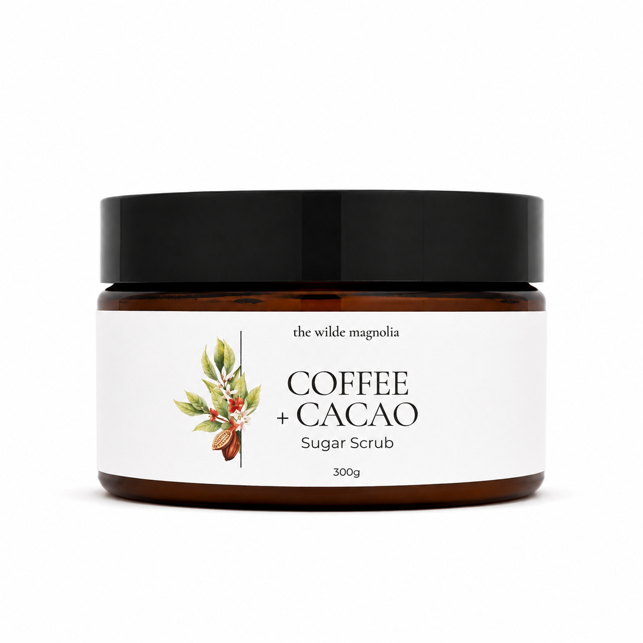 A 300g jar of 'the wilde magnolia' Coffee + Cacao Sugar Scrub. The product is in an amber brown jar with a black lid and a white label featuring a coffee and cacao botanical illustration.