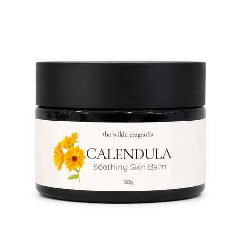 A black jar of 'the wilde magnolia' Calendula Soothing Skin Balm with a white label featuring yellow calendula flowers, set against a plain white background.