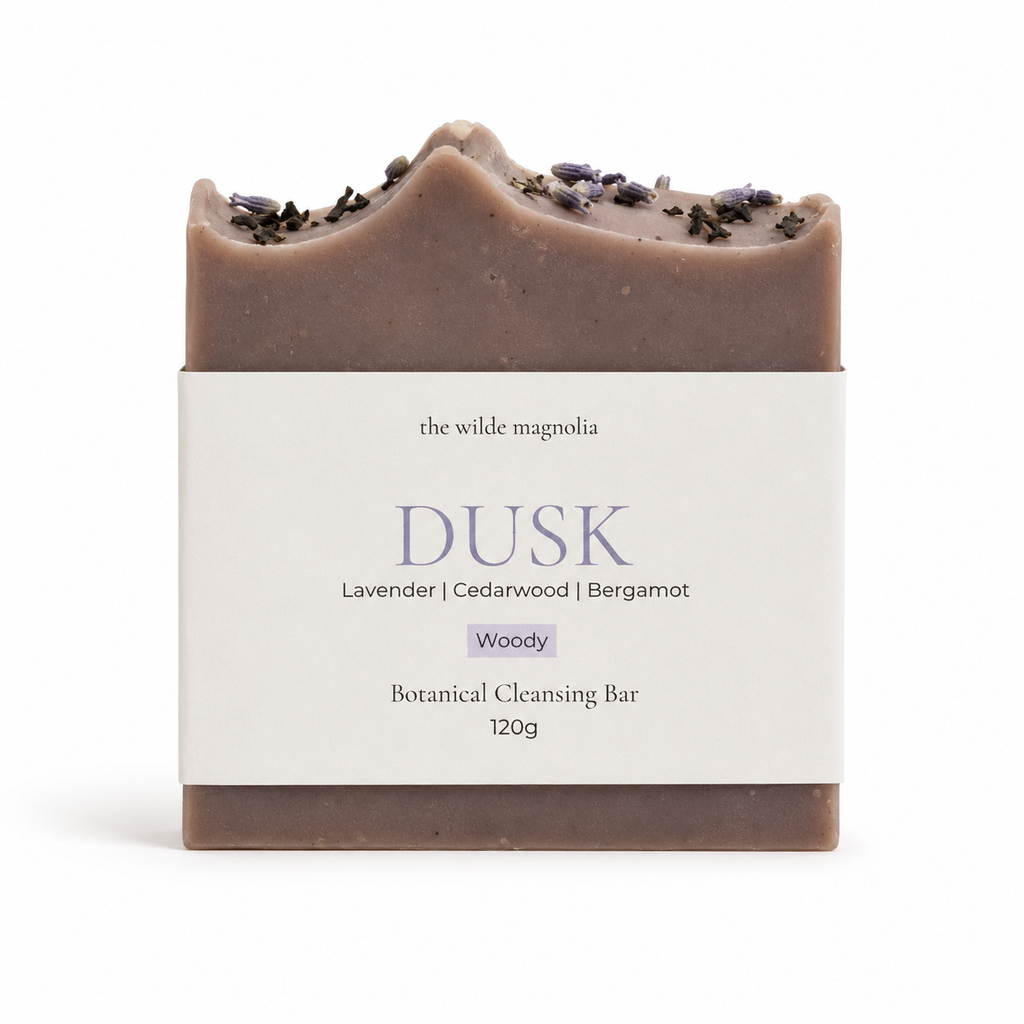 A single botanical cleansing bar wrapped in a white paper label, photographed on a clean white background. The bar is a muted dusty mauve-brown with dried lavender on top.