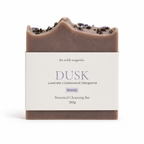 A single botanical cleansing bar wrapped in a white paper label, photographed on a clean white background. The bar is a muted dusty mauve-brown with dried lavender on top.
