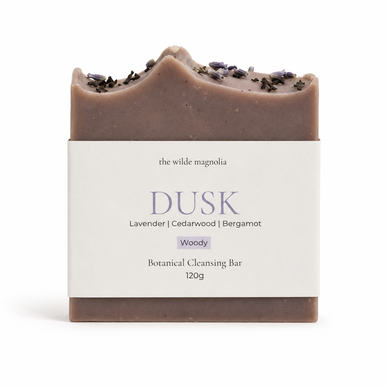 A single botanical cleansing bar wrapped in a white paper label, photographed on a clean white background. The bar is a muted dusty mauve-brown with dried lavender on top.