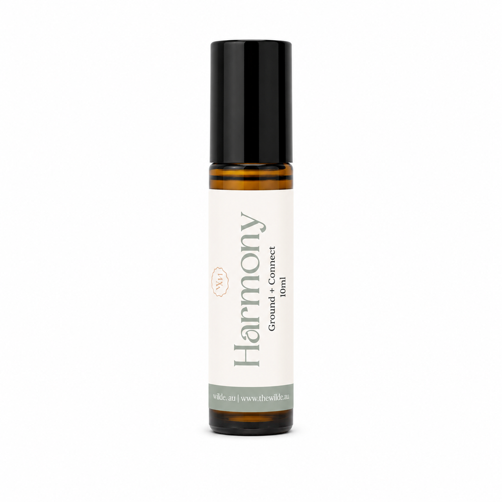 A 10ml amber glass rollerball bottle with a black cap, and a cream-colored label. The label features the brand name 'the wilde magnolia' and the scent name 'Harmony'.