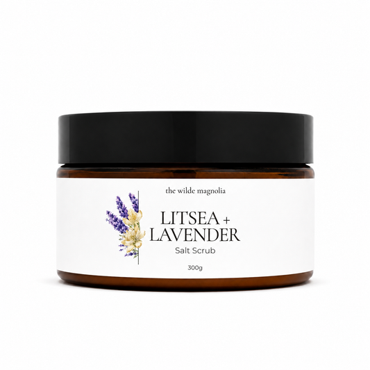 A 300g jar of 'Litsea + Lavender' salt scrub by 'The Wilde Magnolia'. The product is in an amber glass jar with a black lid and a white label featuring purple and yellow lavender illustrations.