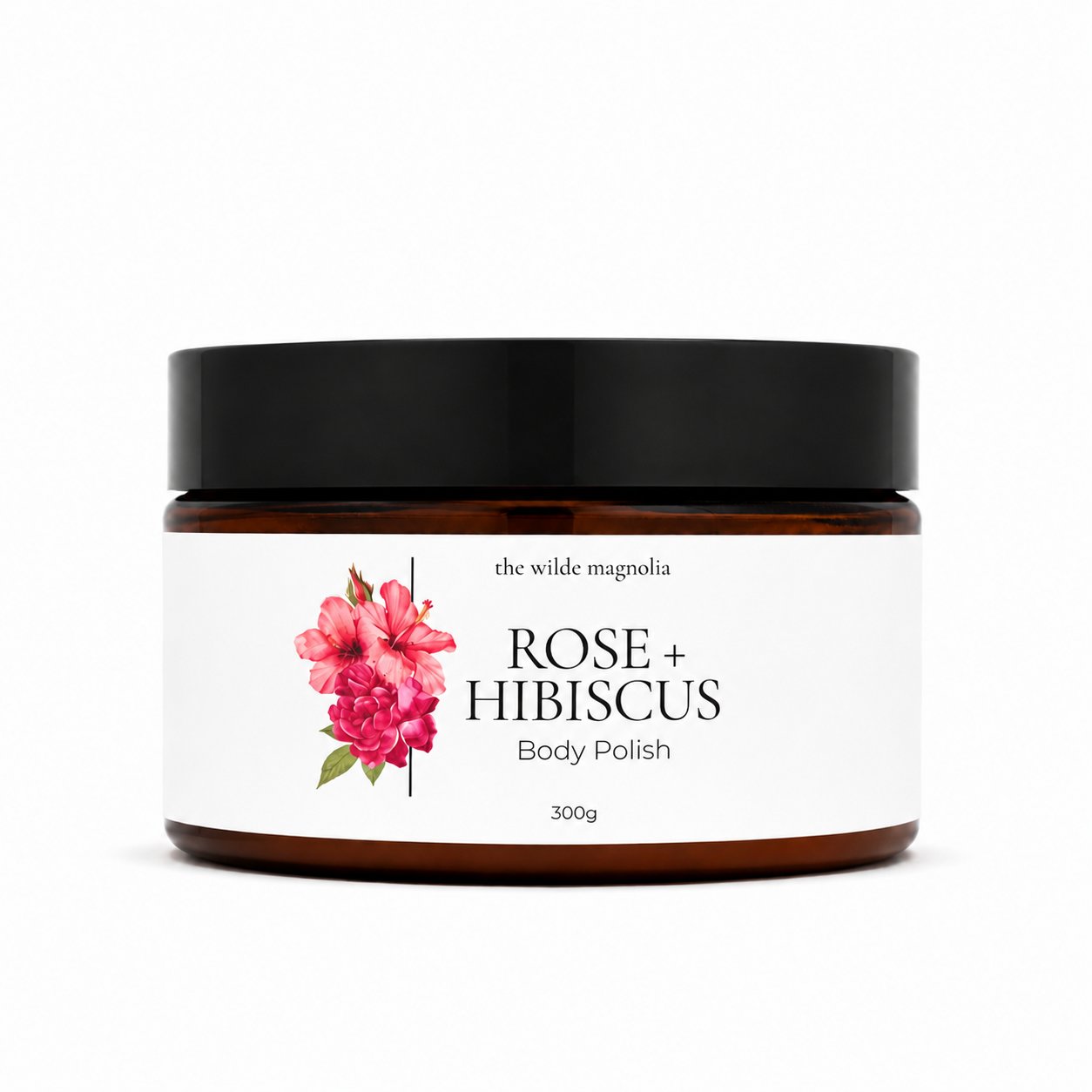 An amber glass jar of 'the wilde magnolia' Rose + Hibiscus Body Polish with a black lid and a white label featuring pink hibiscus flowers, set against a plain white background.