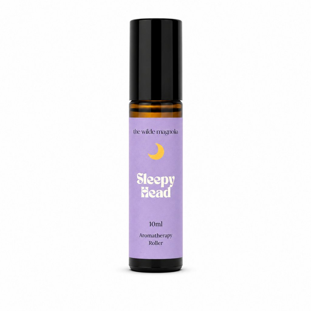 A 10ml roll-on bottle of 'Sleepy Head' aromatherapy oil by 'the wilde magnolia'. The product features a  purple blue label with a yellow crescent moon graphic and white text, housed in an amber glass bottle with a black cap, set against a plain white background.