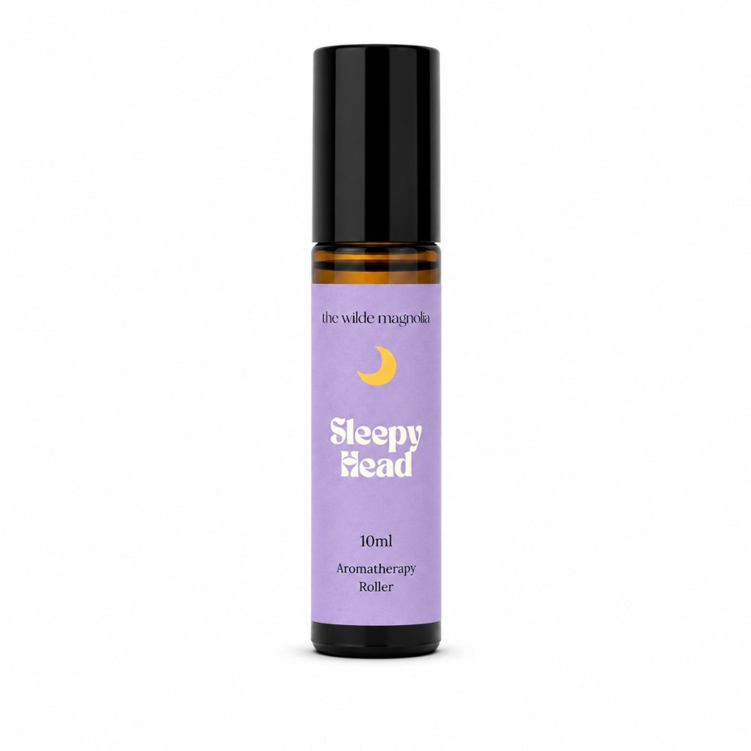 A 10ml roll-on bottle of 'Sleepy Head' aromatherapy oil by 'the wilde magnolia'. The product features a  purple blue label with a yellow crescent moon graphic and white text, housed in an amber glass bottle with a black cap, set against a plain white background.