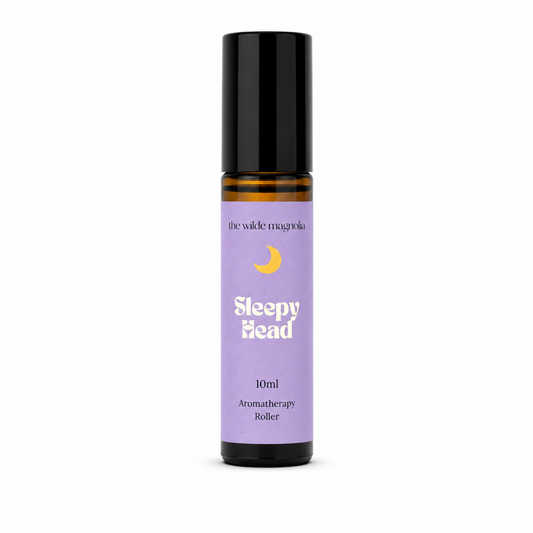 A 10ml roll-on bottle of 'Sleepy Head' aromatherapy oil by 'the wilde magnolia'. The product features a  purple blue label with a yellow crescent moon graphic and white text, housed in an amber glass bottle with a black cap, set against a plain white background.