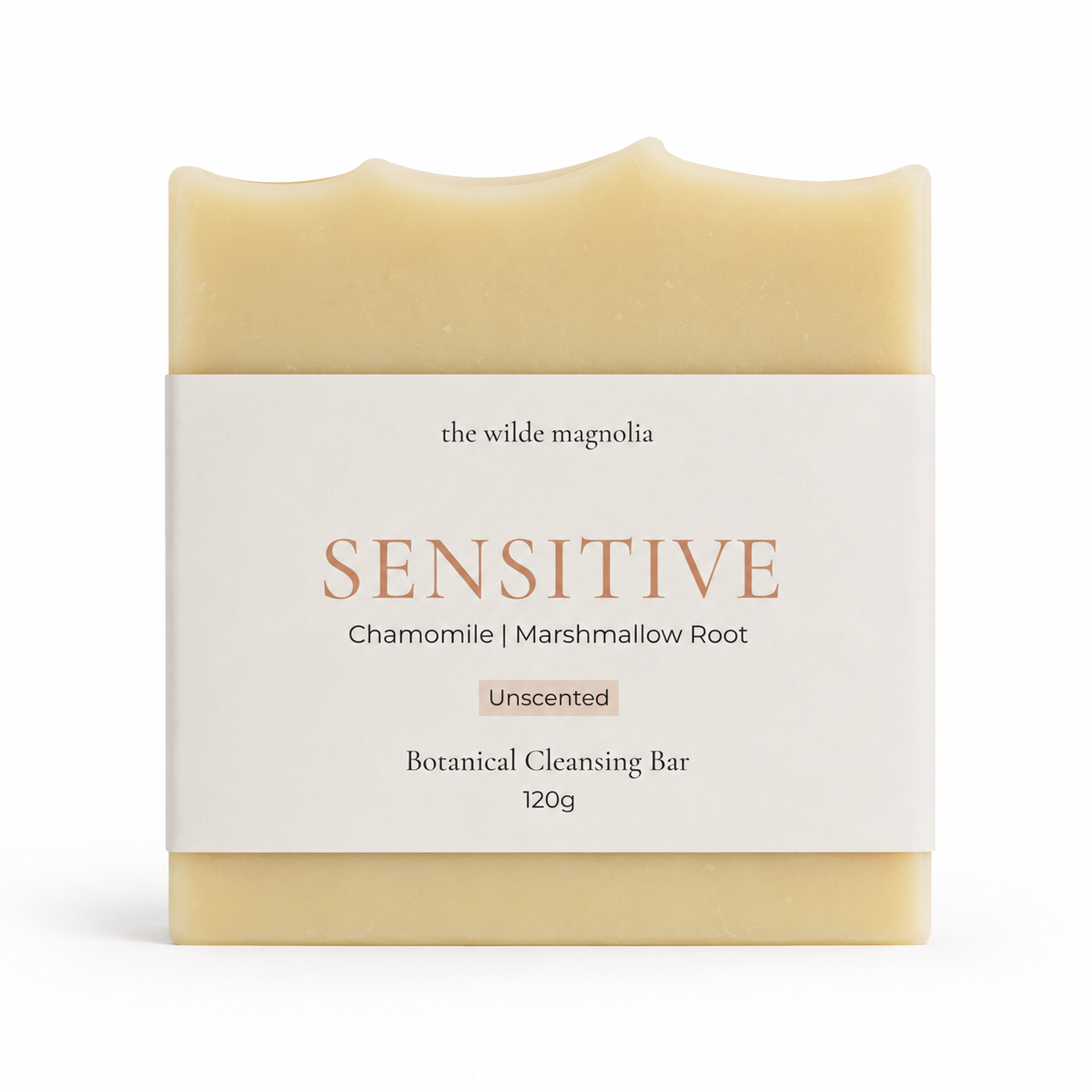 A rectangular bar of botanical cleansing soap from 'The Wilde Magnolia' wrapped in a white paper label that reads 'Sensitive, Chamomile and Marshmallow Root.' The soap itself is a pale, warm yellow-beige.