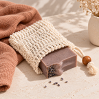 Purple soap in a sisal soap saver bag  on a stone background with a terracotta coloured towel