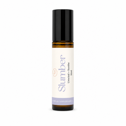 A 10ml amber glass roller bottle of 'Slumber' Unwind + Soothe essential oil from 'the wilde magnolia' with a black cap and a cream-colored label, shown on a plain white background.