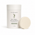 A white cylindrical container of 'the wilde magnolia' Tea Tree + Eucalyptus Shower Steamers, shown next to a single round, textured off-white steamers disc on a clean white background.