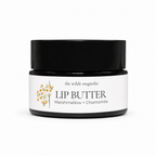 An amber jar of lip butter with a white label reading 'the wilde magnolia LIP BUTTER Marshmallow + Chamomile' and a small floral illustration, photographed on a clean white background.